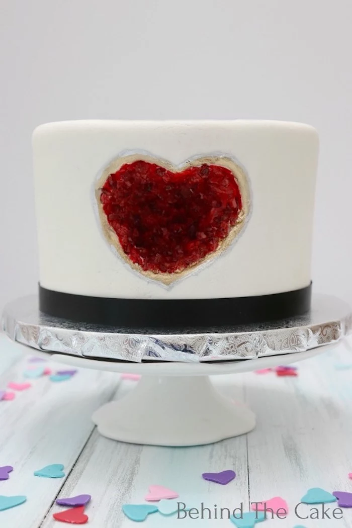one tier cake, covered with white fondant, decorated with heart shaped red rock candy, amethyst cake, placed on white cake stand