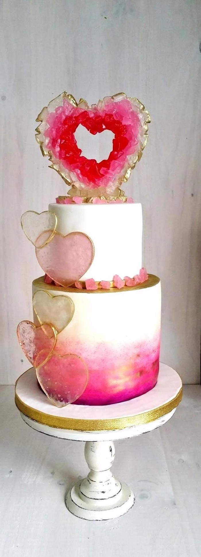geode cake recipe, two tier cake, covered with pink and white fondant, decorated with pink heart shaped rock candy