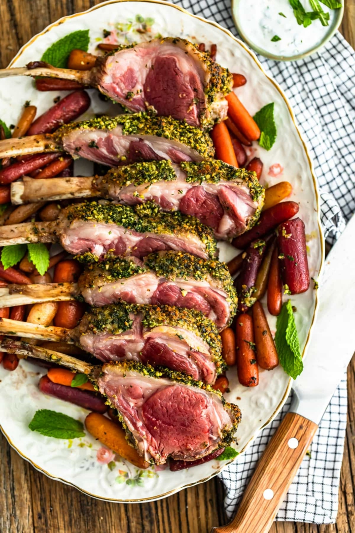 sliced rack of lamb, arranged on a white palte, roasted baby carrots around it, easter meal ideas