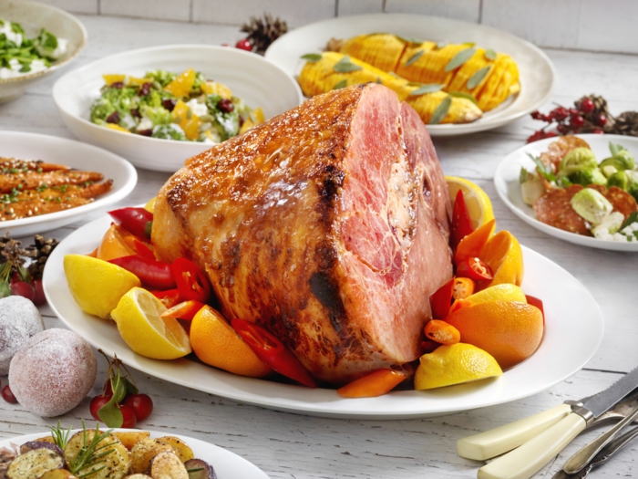 baked ham on white plate, traditional easter food, halved lemons and peppers arranged around it