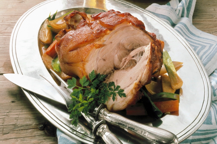 baked ham on metal plate, traditional easter food, stemaed vegetables around it, knife and fork on the side