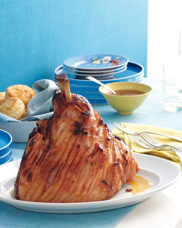 large piece of meat, placed on white plate, traditional easter food, table with blue table cloth and plates on it