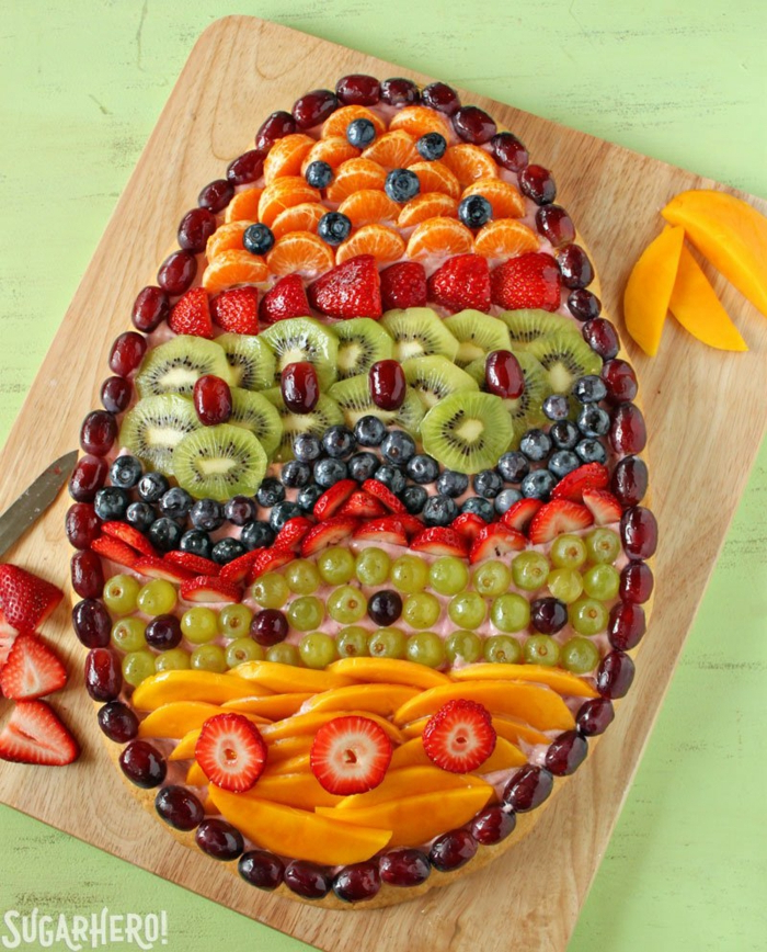 traditional easter food, dfferent fruits arranged in the shape of an egg, wooden cuttin board