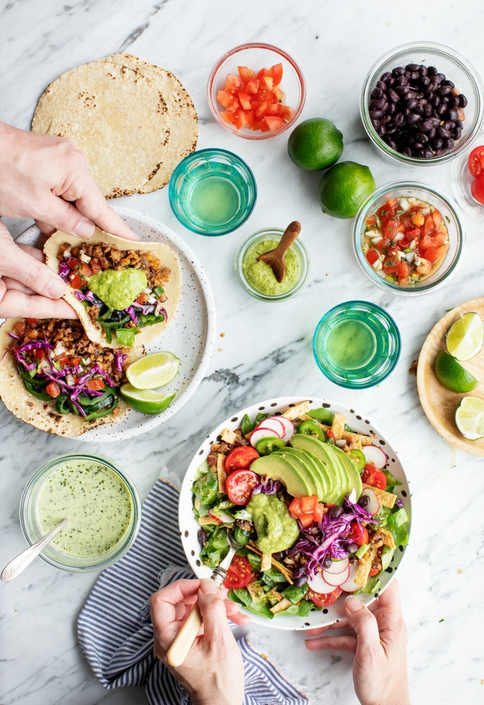 green salad wit avocado and tomatoes, different ingredients for tacos on marble table, easy dinners for two