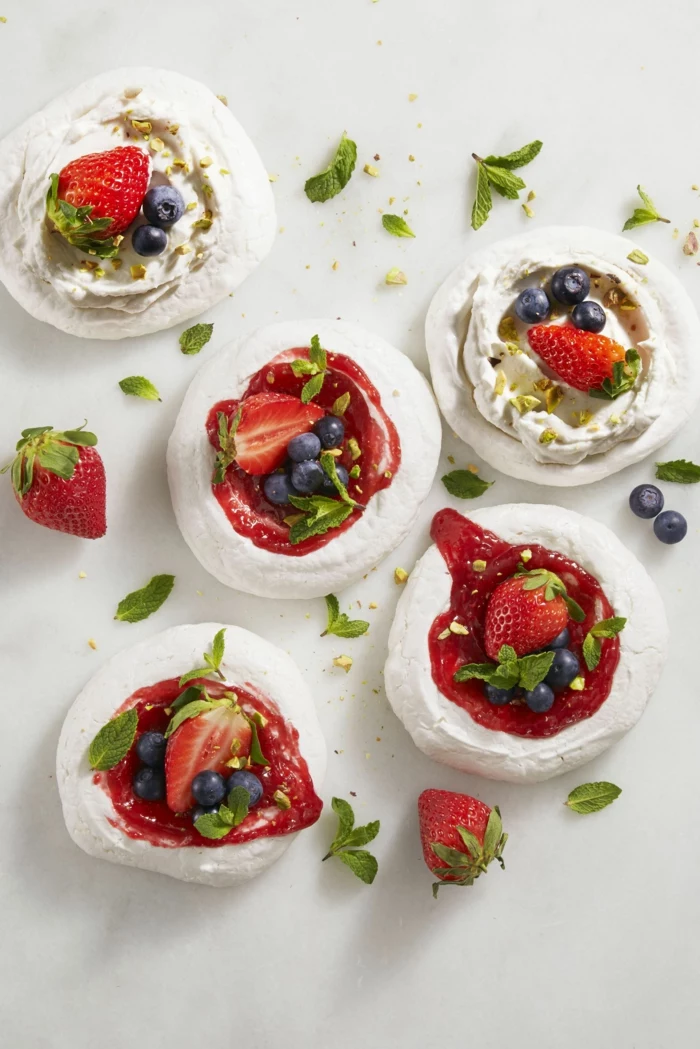 mini pavlovas, easter dinner ideas 2019, strawberries and blueberries on top, arranged on white surface