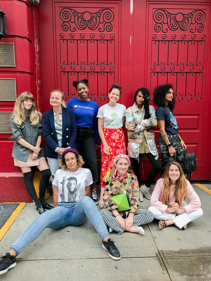 a large group of girls posing for a photo, large red door behind them, dressed in different outfits, middle school outfits