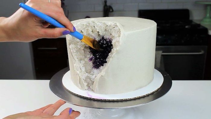one tier cake, covered with white fondant, crystal cake, white rock candy painted in purple, placed on silver cake stand