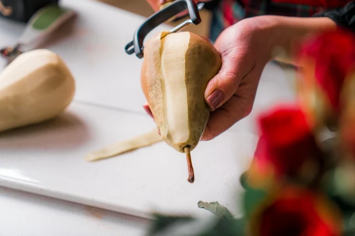 poached pears, pear being peeled with black julienne peeler, white cutting board