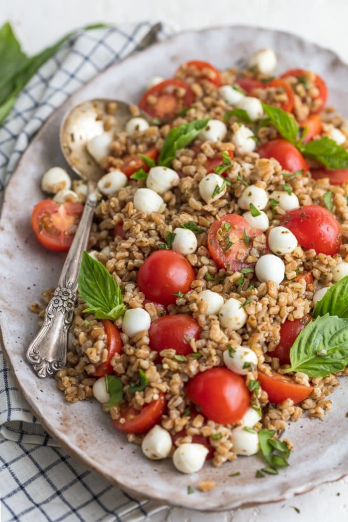 caprese salad with couscous, traditional easter dinner, basil leaves garnish, halved cherry tomatoes and baby mozzarella