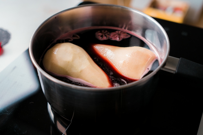 cinnamon sticks and star anise in red wine, simmering in metal sauce pan, two pears inside, poached pears