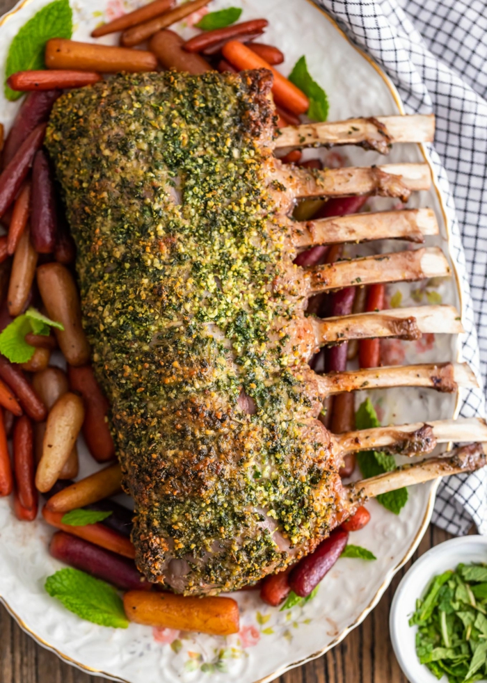 garlic and herb rack of lamb, placed on white plate, easter meal ideas, roasted baby carrots around it