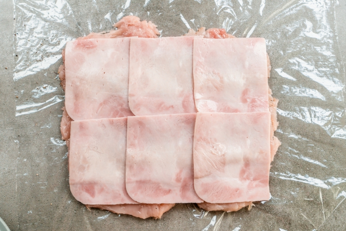 six slices of ham arranged on top of chicken breast, placed on foil on grey countertop, chicken cordon bleu recipe