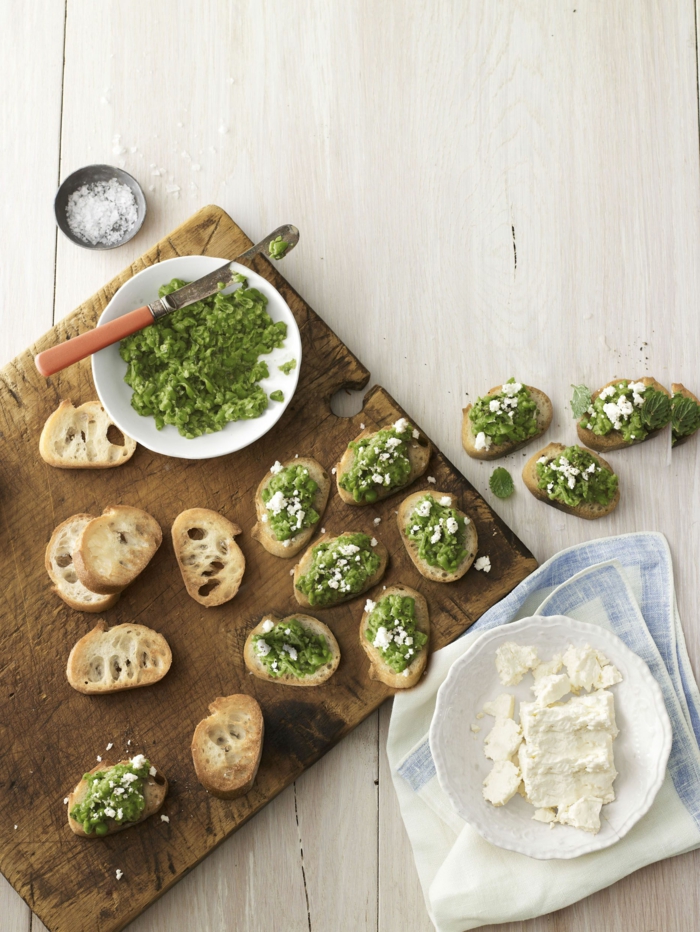 easter ham dinner, small bread bites with pesto spread, crumbled feta cheese, on wooden cutting board