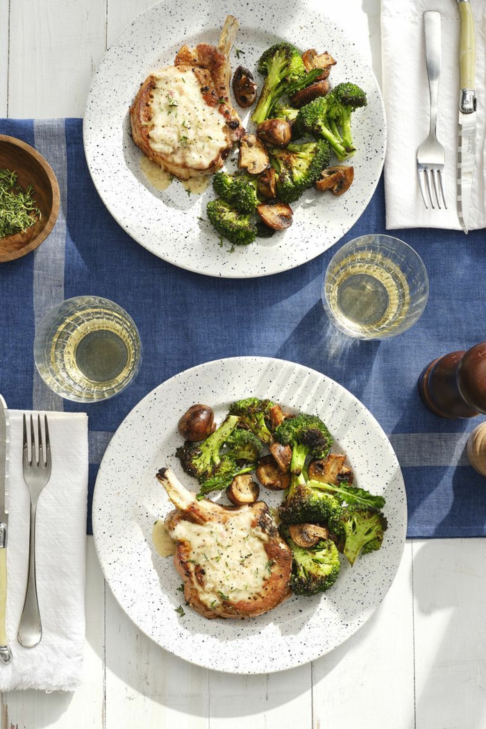 two white plates placed on blue table cloth, easter ham dinner, smothered pork chops with steamed broccoli and mushrooms on the side