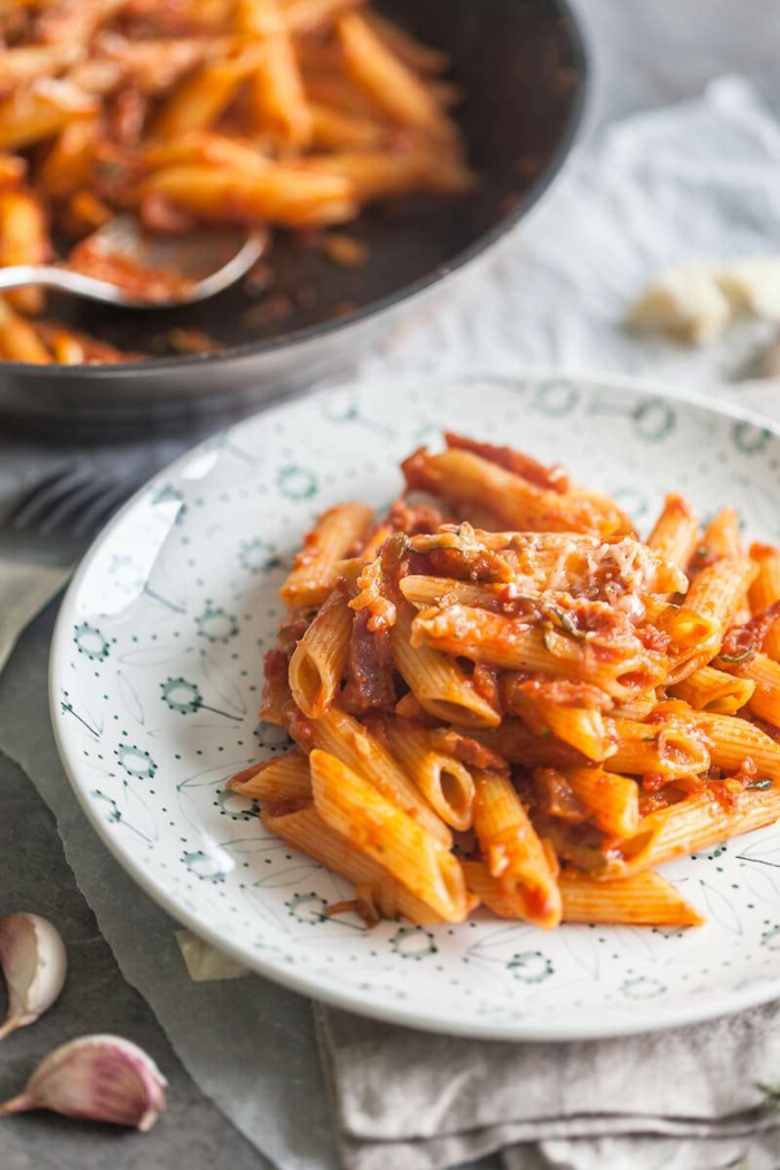 spicy penne, grated parmesan on top, dinner ideas for tonight, placed on white plate, garlic cloves on the side