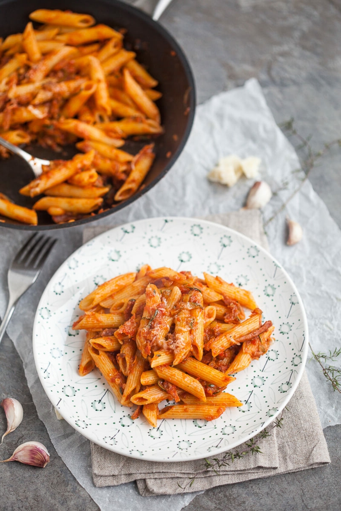 easy weeknight dinners, spicy penne, grated parmesan cheese on top, placed in white plate, sauce pan on the side