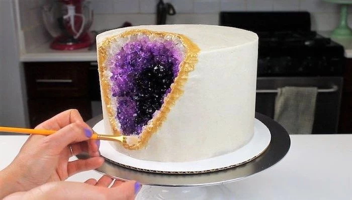 one tier cake, covered with white fondant, decorated with rock candy, painted in purple and gold, crystal cake