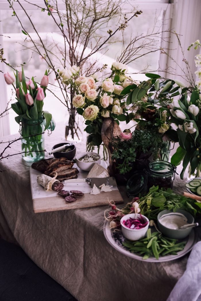 table full bouquets with different flowers, easter ham dinner, ham and cheese placed on wooden cutting board