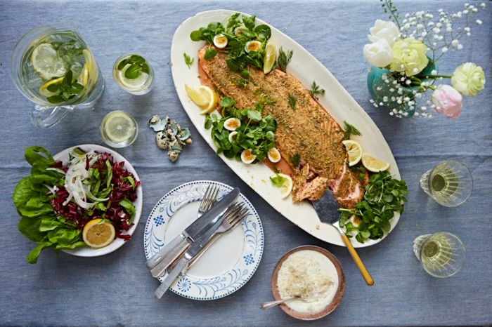 easter dinner menu ideas, table with blue table cloth on it, baked salmon placed on white plate, green herbs on the side