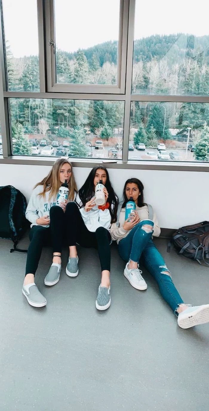 three girls sitting on the floor, wearing jeans and sweatshirts, cute high school outfits, white and grey vans shoes