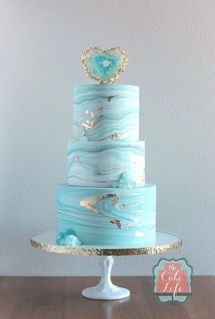 three tier cake, covered with blue and white marble fondant, decorated with turquoise rock candy, pink geode cake