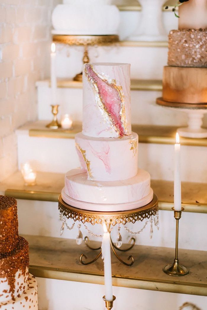 three tier cake, covered with pink marble fondant, pink geode cake, decorated with pink rock candy, placed on gold cake stand