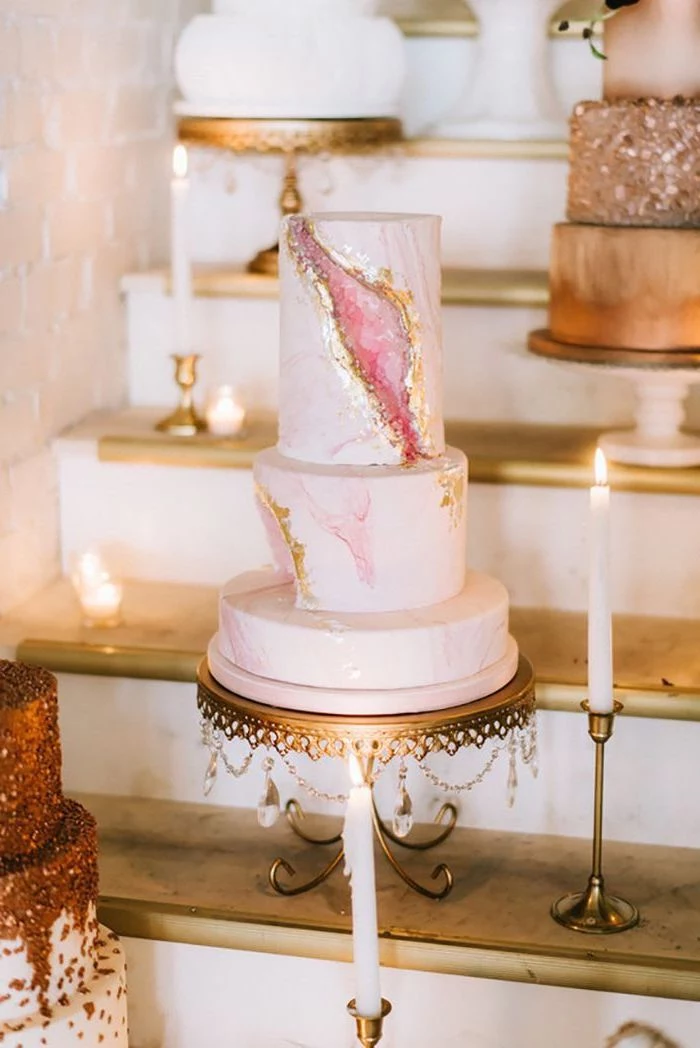 three tier cake, covered with pink marble fondant, pink geode cake, decorated with pink rock candy, placed on gold cake stand