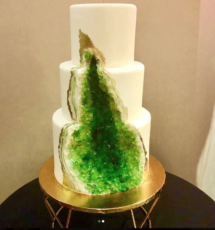three tier cake, covered with white fondant, pink geode cake, decorated with green rock candy, placed on gold cake stand