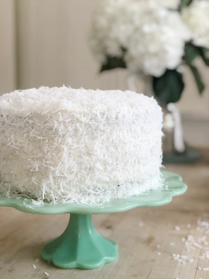 one tier cake, covered with coconut flakes, palced on turquoise cake stand, easter dinner menu ideas