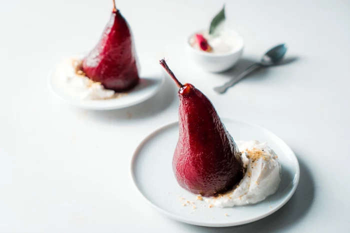 poached pears in red wine, served with cream on white plates, placed on white countertop