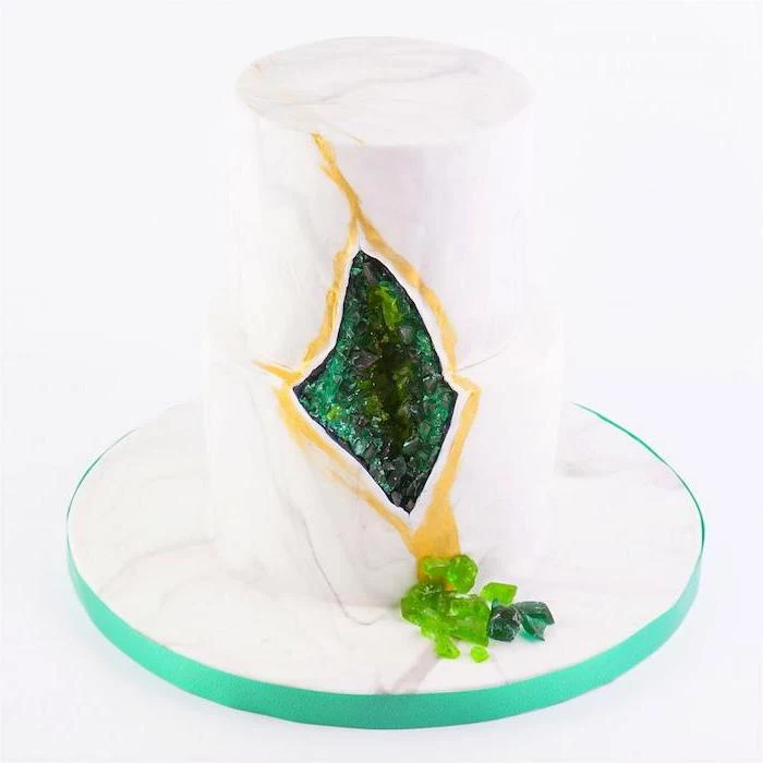 two tier cake, covered with white fondant, what is a geode cake, decorated with green rock candy and gold paint