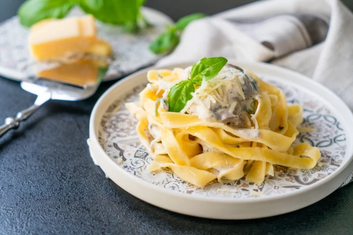 black surface, tagliatele recipe, white plates, garnish of creamy mushroom sauce, parmesan cheese and basil leaves
