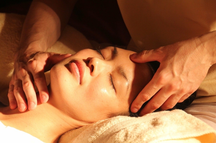 woman laying on a bed with closed eyes, white towel under hear head, spa holidays, getting a massage