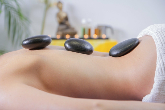 woman laying in bed, wrapped in white towel, three rocks on her back, spa holidays