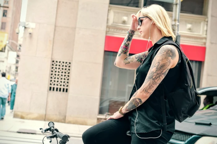 neo traditional tattoo, blonde woman riding a bike, wearing all black, arms covered with tattoos