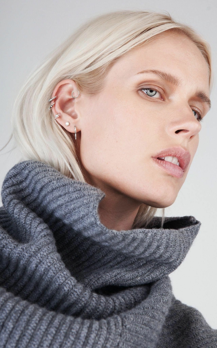 blonde woman with blue eyes, wearing grey turtleneck sweater, double cartilage piercing, multiple earrings