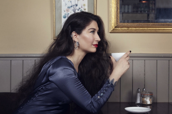 woman with long black wavy hair, wearing blue satin dress, double helix piercing, holding a coffee cup