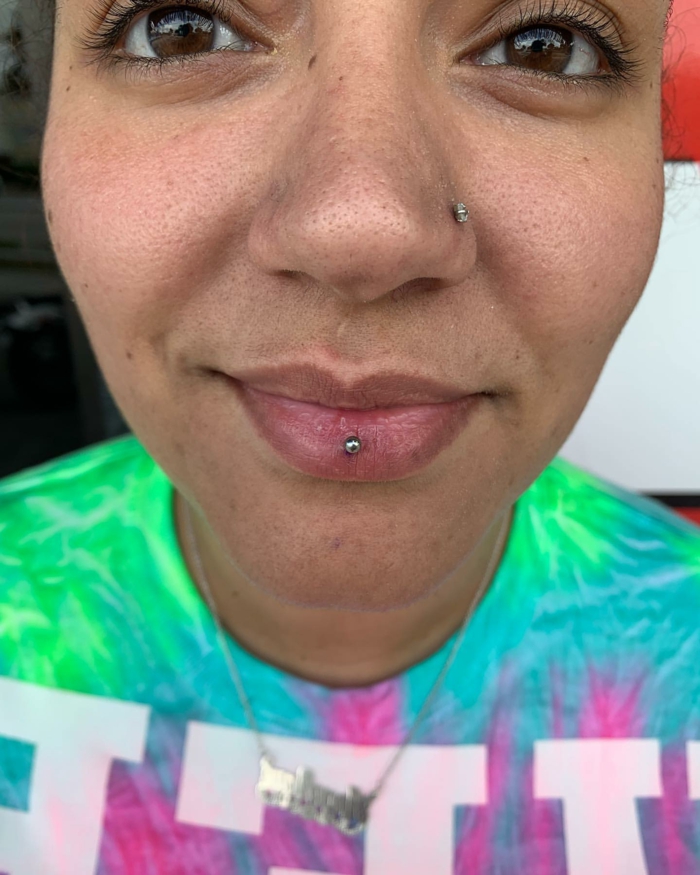 close up photo of woman with brown eyes, middle lip piercing, lips with no lip gloss, nose piercing