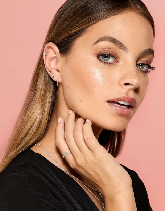 woman with brown hair and blue eys, cartilage piercing, weaering black velvet top, pink background