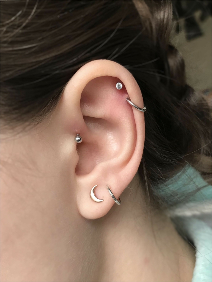 multiple earrings on an ear, close up photo of an ear, cartilage piercing, woman with brown hair