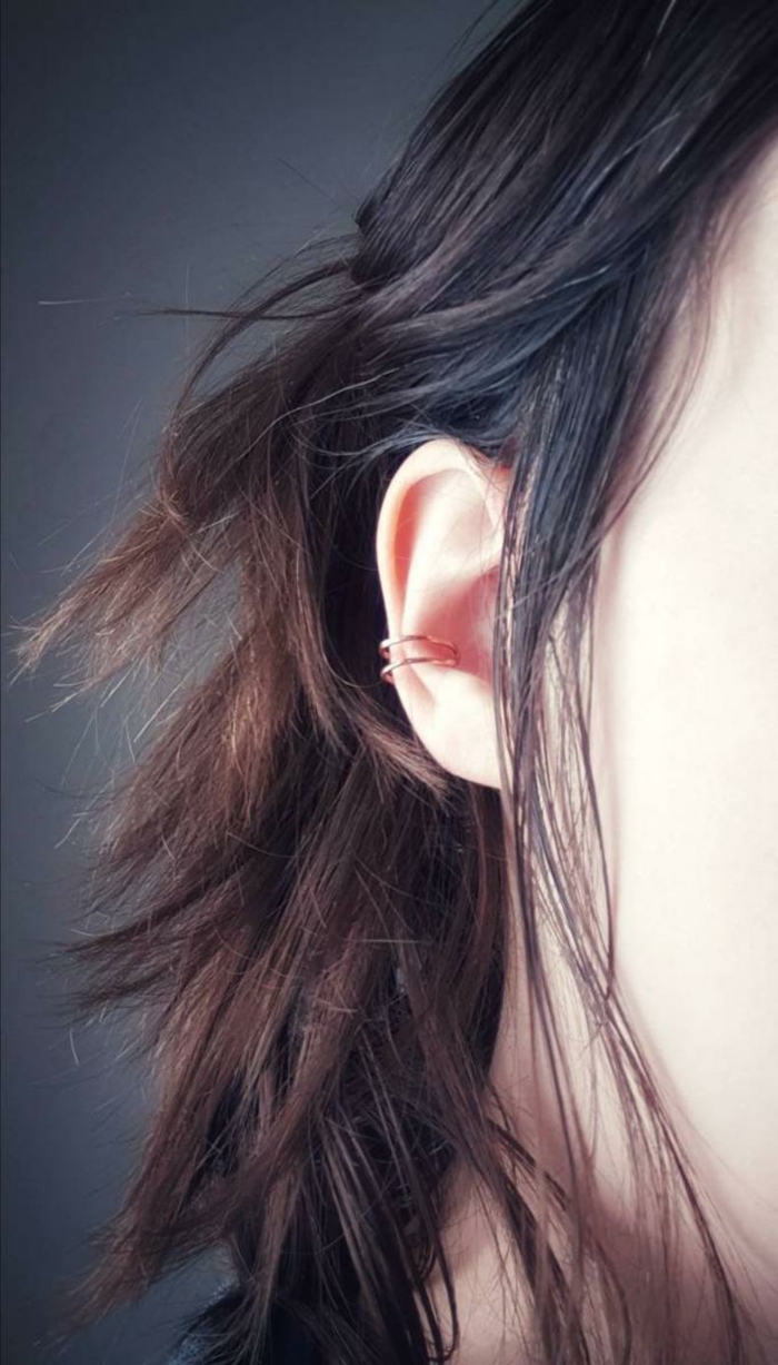 close up photo of an ear, woman with brown wavy hair, cartilage ear piercings, golden ring earrings