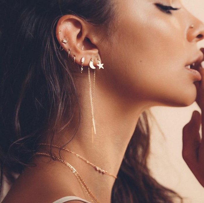 woman with brown wavy hair, forward helix piercing, multiple golden earrings, nose piercing