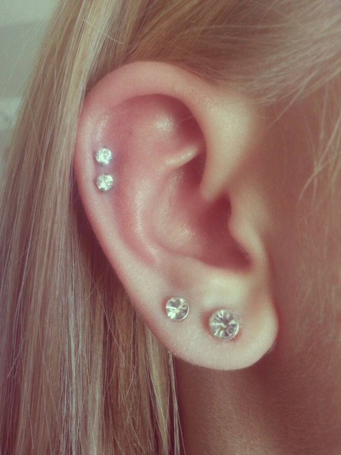 woman with blonde hair, wearing four earrings with rhinestones, forward helix piercing, close up photo