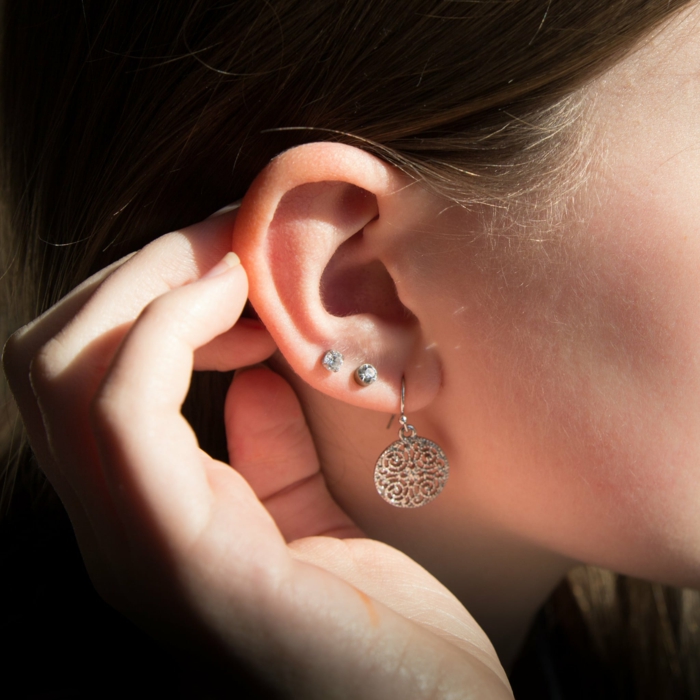 forward helix piercing, close up photo of an ear, woman with brown hair, wearing earrings with rhinestones