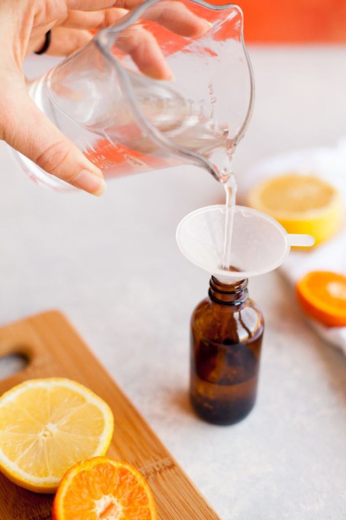 antibacterial gel poured into small brown bottle, lemon slices on the side on wooden cutting board, hand sanitizer ingredients