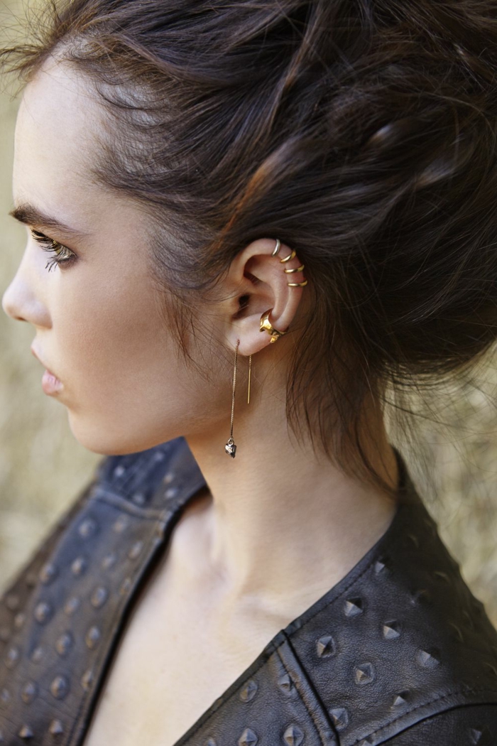 woman with brown hair, wearing black leather jacket, helix piercing, multiple golden earrings on her ear