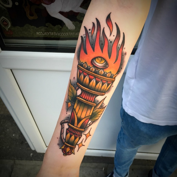 forearm tattoo, flaming torch with an eye in the flames, traditional tattoo ideas, man wearing jeans