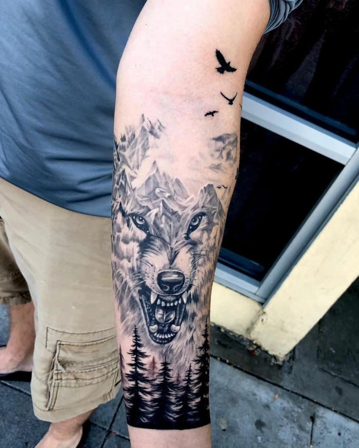 forearm tattoo, wolf head as a mountain range, trees underneath, mountain tattoo, birds flying