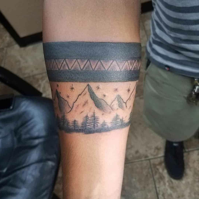 hiking tattoos, mountain range with trees, black armband going around the arm, forearm tattoo