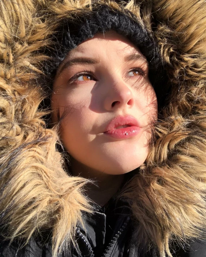 girl with brown eyes, ooking up at the sun, wearing a large hood, labret piercing, black beanie